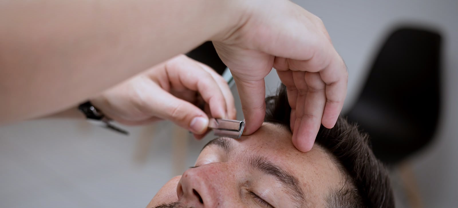 Design de sobrancelha masculina sendo feito com pinça na Barbearia Ribas
